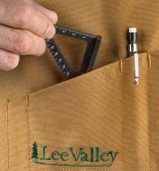A woodworker slips a Veritas 60mm Pocket Layout Square into the pocket of a workshop apron