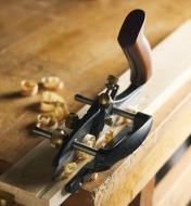 A small plow plane on a board with a groove and wood shavings