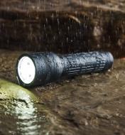 A flashlight is on a rock, in the rain