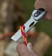 Using the 3-in-1 knife with the 2 3/4"" scalloped-edge blade to cut a piece of rope