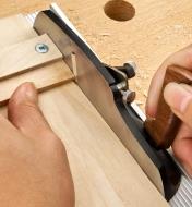 Personne taillant le bout d’une petite pièce de bois avec un rabot pour planche à recaler miniature et une planche à recaler