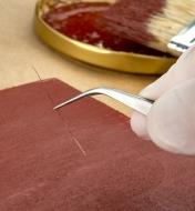 Using a pair of forceps to remove a loose paintbrush bristle from a freshly painted wooden panel