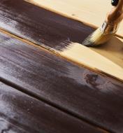 Using a brush to apply Osmo rosewood decking oil to a wooden deck