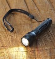 A Q2 flashlight with light on and an attached lanyard on a wood surface