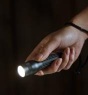 A person holding a flashlight with the lanyard attached to their wrist