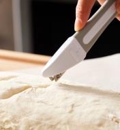 Using a blade set in the lame’s straight blade holder to pierce the skin of proofed bread dough