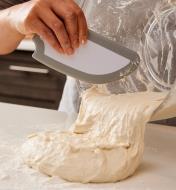Placing fresh dough on a floured countertop, using a bowl scraper to remove it from a mixing bowl