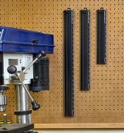 Three sizes of metric shop rules hung on a pegboard workshop wall near a drill press