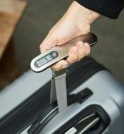 A digital luggage scale fastened to a suitcase to measure the weight