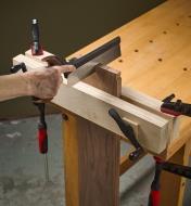 A saw cutting a board that is held in a vise with two press screws