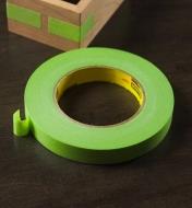A roll of green binding tape next to a taped wooden frame