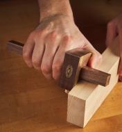 A mortise marking gauge being held at an angle on a board