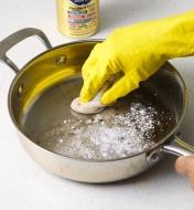 Using a damp cloth and Bar Keeper’s Friend to clean a pan’s cooking surface