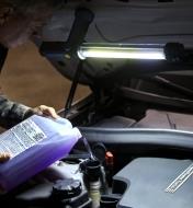 Refilling a car’s windshield-washer fluid, lit by an LED tube light held magnetically under the hood