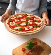 An uncooked pizza on a pizza stone, with sauce, bocconcini, tomatoes and fresh basil toppings