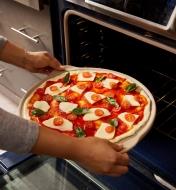 An uncooked pizza being placed in an oven on a ceramic pizza stone