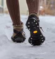A person walking on a snowy path wearing Icers on their boots