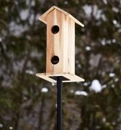 A wooden birdhouse mounted to the top of a garden pole outdoors