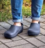 A woman wears European garden clogs while standing on an outdoor walkway made of interlocking pavers