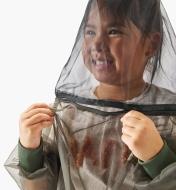 A child wearing a hooded bug-protection shirt opens a zipper at the neck