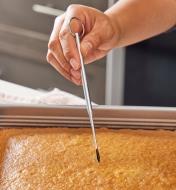 A cake tester being inserted into a sheet cake