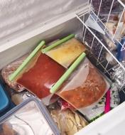 Three sizes of reusable silicone bags filled with food in a freezer