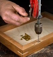 Using a hand brace and an HSS drill bit to drill holes for mounting hinges on a wooden box lid