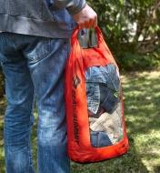 A person in an outdoor setting carries a 20 litre dry sack filled with clothes