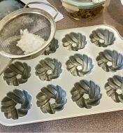 Dusting the inside of a mini Bundt pan with flour so the cakes release neatly after baking
