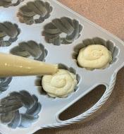 Using a piping bag to fill a mini Bundt pan with cake batter