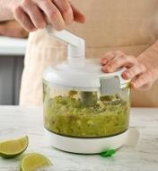 The handle of a manual food processor is being turned to puree and mix ingredients