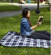 Personne qui lit un livre assise sur une couverture d'extérieur doublée à carreaux