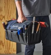 A person carries a carpenter’s tool bag holding a level, a file, a chisel and other tools