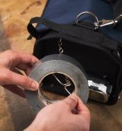 A person accesses a roll of tape held on the T-bar at one end of a carpenter’s tool bag