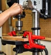 Ratcheting clamps holding a wooden panel to a drill press