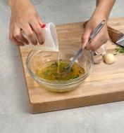 A cook pours oil from a silicone mini-measure into a bowl to make salad dressing