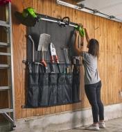 A string-trimmer being attached to a hanging organizer that is holding outdoor tools