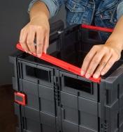 A person sets reinforcing brackets on the walls of a collapsible cart to help them hold their shape