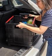 A person loads a collapsible cart filled with groceries into a hatchback car