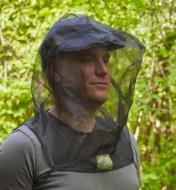 A man wears a bug-protection hood in a woodland setting