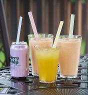 Three drinks in glasses and one in a can, all with different colored straws