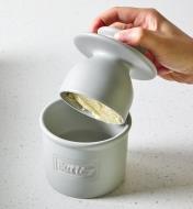 The lid filled with butter being lifted off of the base of a butter bell crock