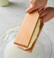 Personne pressant du beurre frais entre deux palettes à beurre au-dessus d'un bol