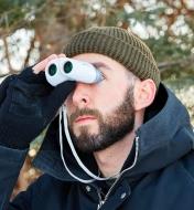 A man in winter gear looking through compact binoculars