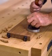 A board supported against two bench dogs being planed on a workbench