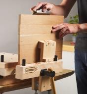 The tool clamp in a vise holding a square board as its edge is being planed