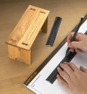 Personne utilisant une règle d'établi pour tracer une ligne sur un bloc de papier quadrillé Veritas devant un petit banc en bois