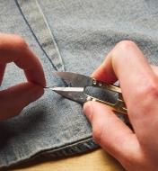 Using a pair of spring shears to trim a loose thread from the seam of a garment