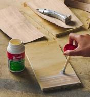 Contact cement being applied to a board with the brush, next to an open container