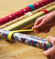 A person taps a slap band against a roll of wrapping paper, causing the band to coil around the roll
